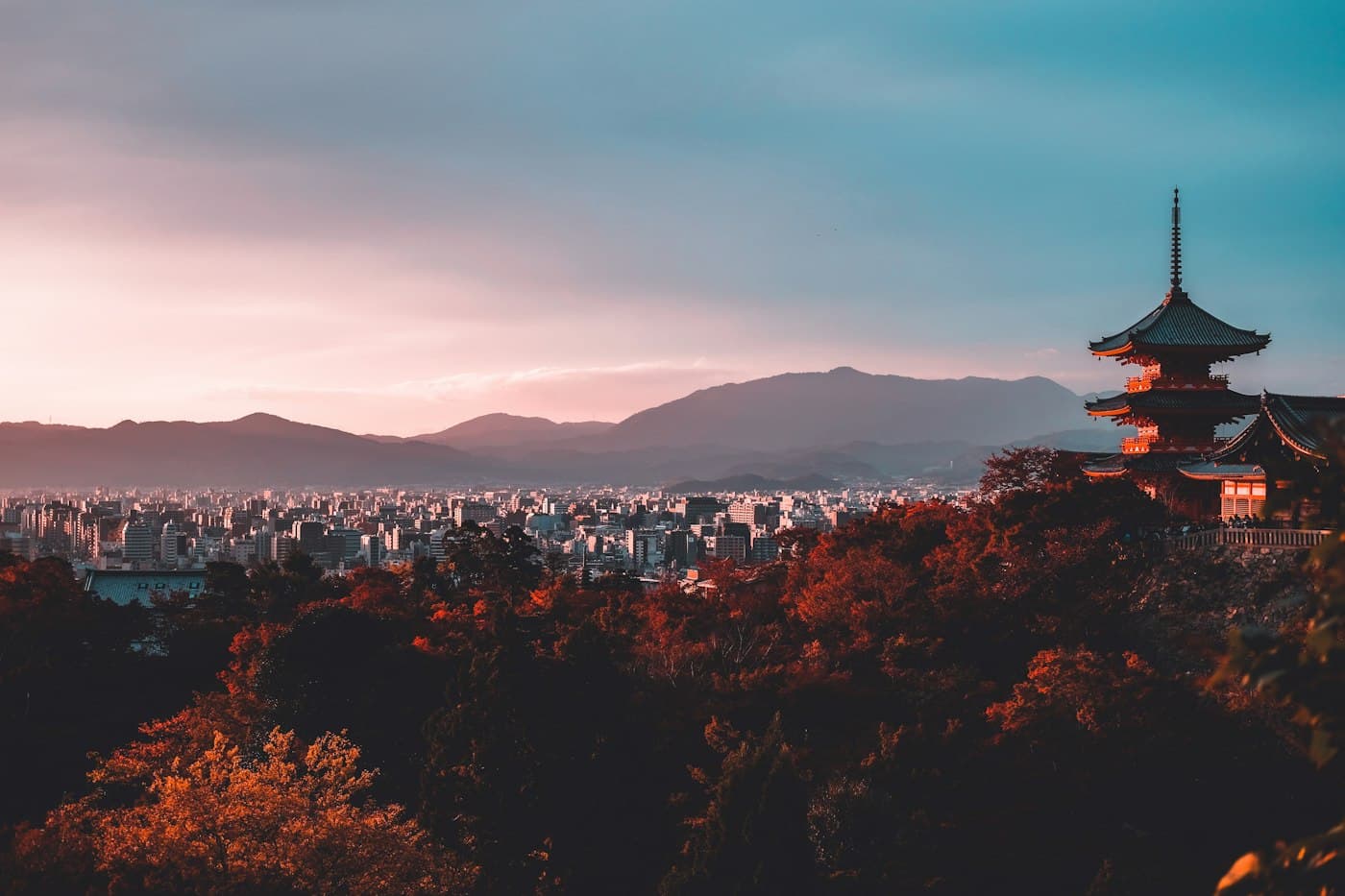 A pagoda above a city at sunset with mountains in the distance, Japan.